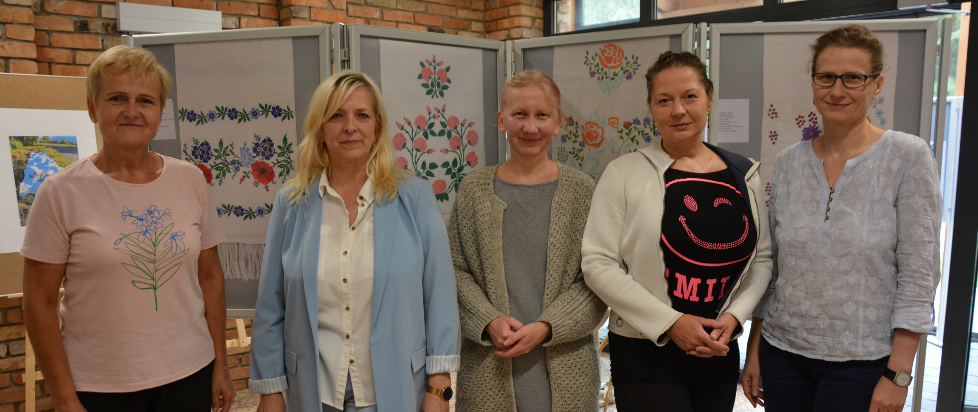 Autorka prac wraz z Wicestarostą Joanną Kojło, Naczelnikiem Wydziału Promocji Walentyną Pietroczuk oraz dwoma uczestniczkami wystawy pozują na tle ekspozycji haftowanych ręczników