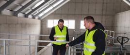 Dwóch mężczyzn w kamizelkach odblaskowych stojących w budynku oczyszczalni ścieków w Skawie