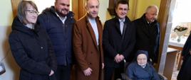 Zdjęcie grupowe - goście jubilatki, ubrani w zimowe kurtki i płaszcze, stoją w szeregu. Przed nimi siostra na wózku
