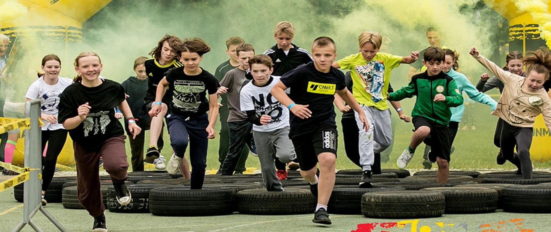 Grupa dzieci przeskakująca przez opony leżące na asfalcie
