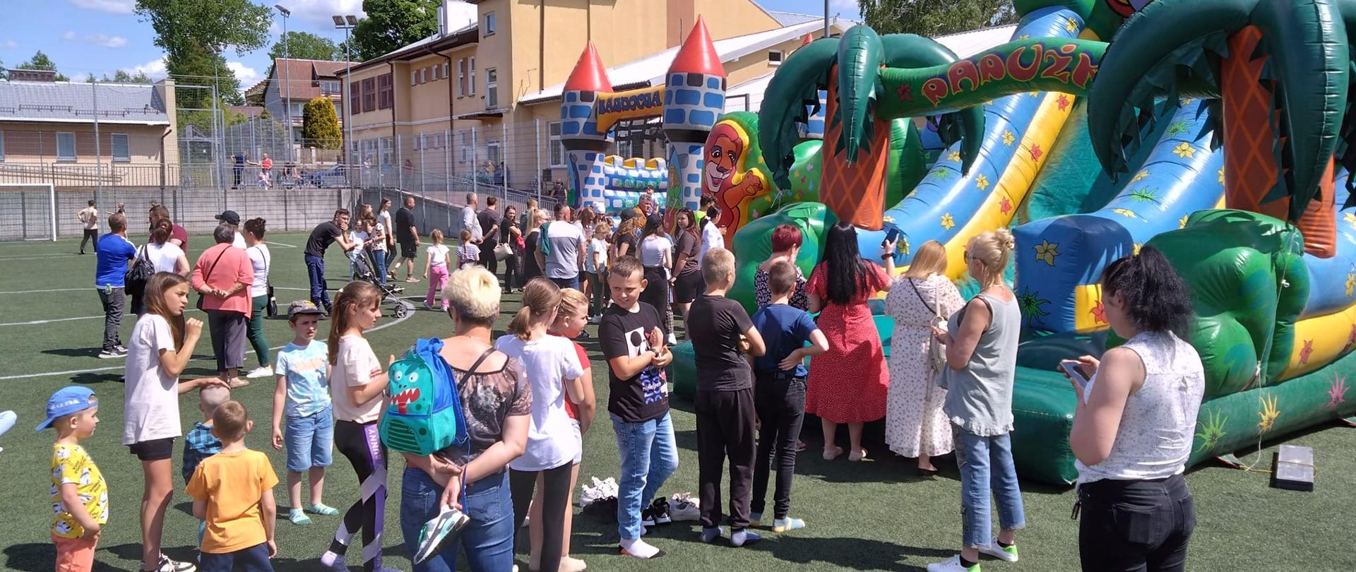 boisko szkolne na nim dmuchany plac zabaw i grupa rodziców z dziećmi.