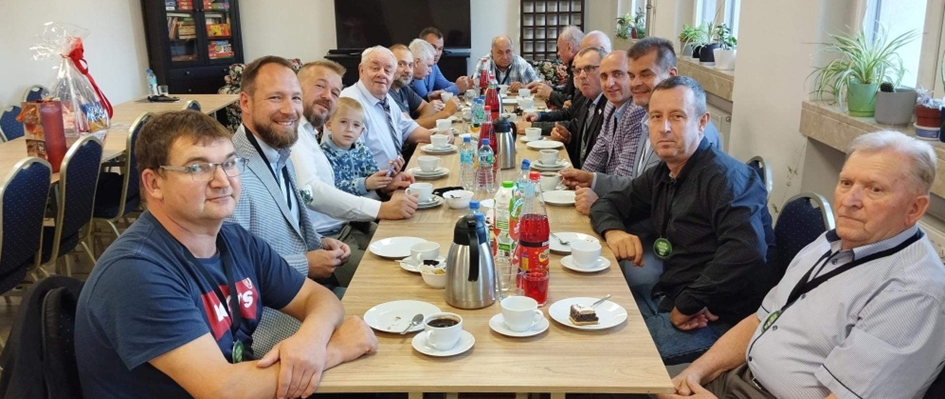 Grupa mężczyzn siedzi przy długim drewnianym stole