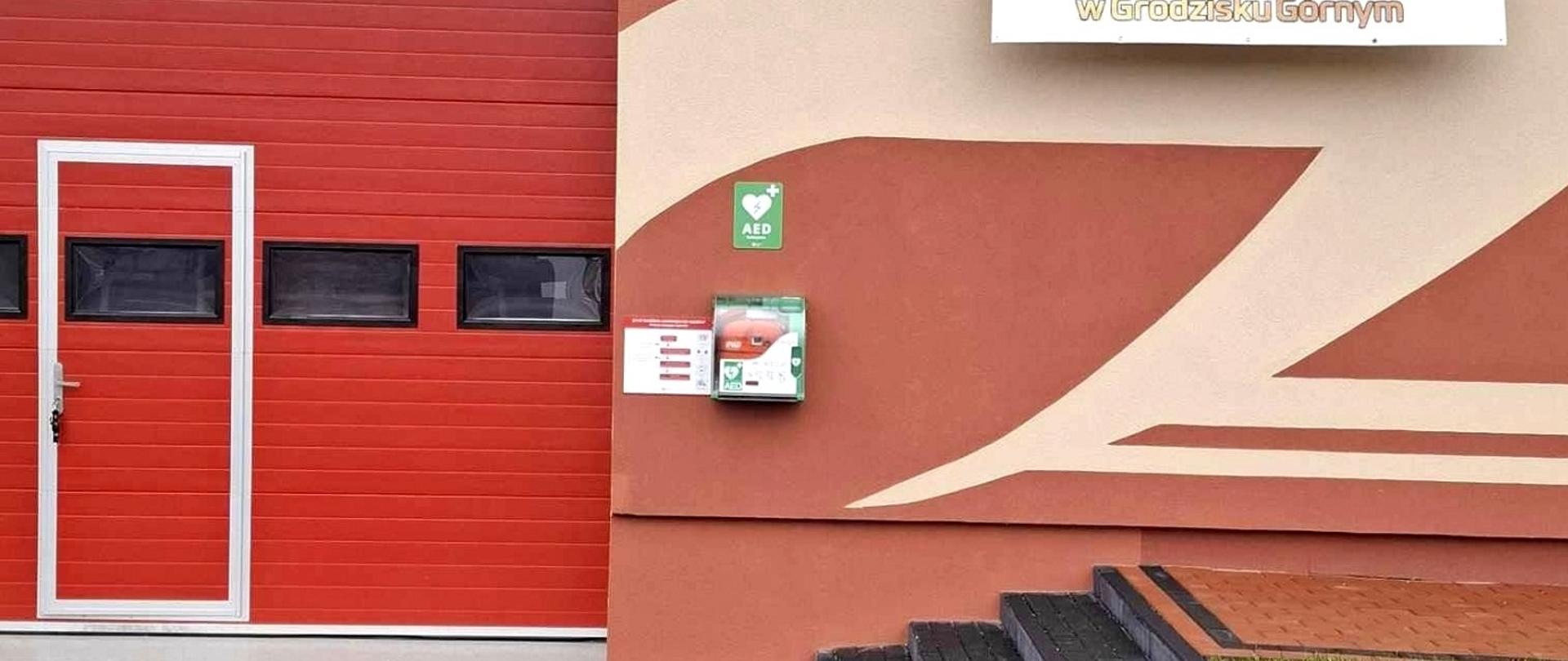 czerwony budynek remizy z czerwoną blachą i czerwonymi drzwiami garażowymi przed budynkiem szara kostka 