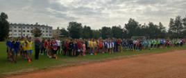 Inauguracja Szkolnego Roku Sportowego 2021/2022 na Stadionie Miejskim w Chorzelach. Fotografia przedstawia uczniów biorących udział w zawodach. Młodzież stoi na murawie boiska podzielona na grupy według płci, wieku oraz szkoły.