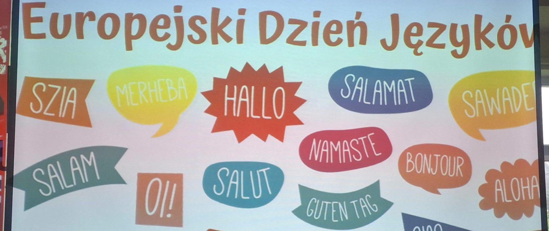 Na zdjęciu widać białą tablicę, a na niej czerwony napis DZIEŃ JĘZYKÓW OBCYCH oraz kolorowe chmurki z DZIEN DOBRY w różnych europejskich językach. 