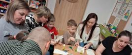 Rodzice z dziećmi siedzą przy stole, przygotowują gwiazdy z papieru
