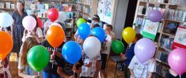 Na zdjęciu widać dzieci trzymające kolorowe balony na patyczkach.