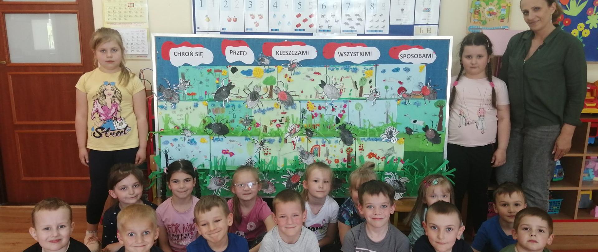Dzieci przy tablicy z rysunkami łąki i kleszczy