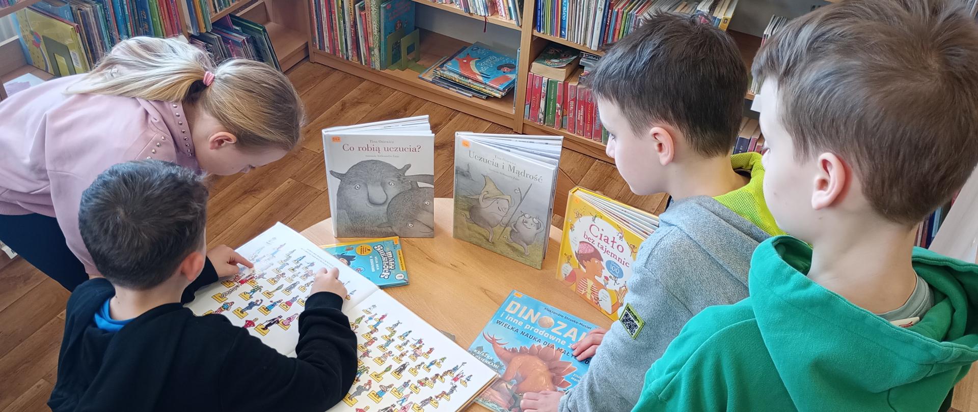 Zdjęcie przedstawia czwórkę dzieci przeglądających książkę z obrazkami w ramach zajęć z przysposobienia bibliotecznego