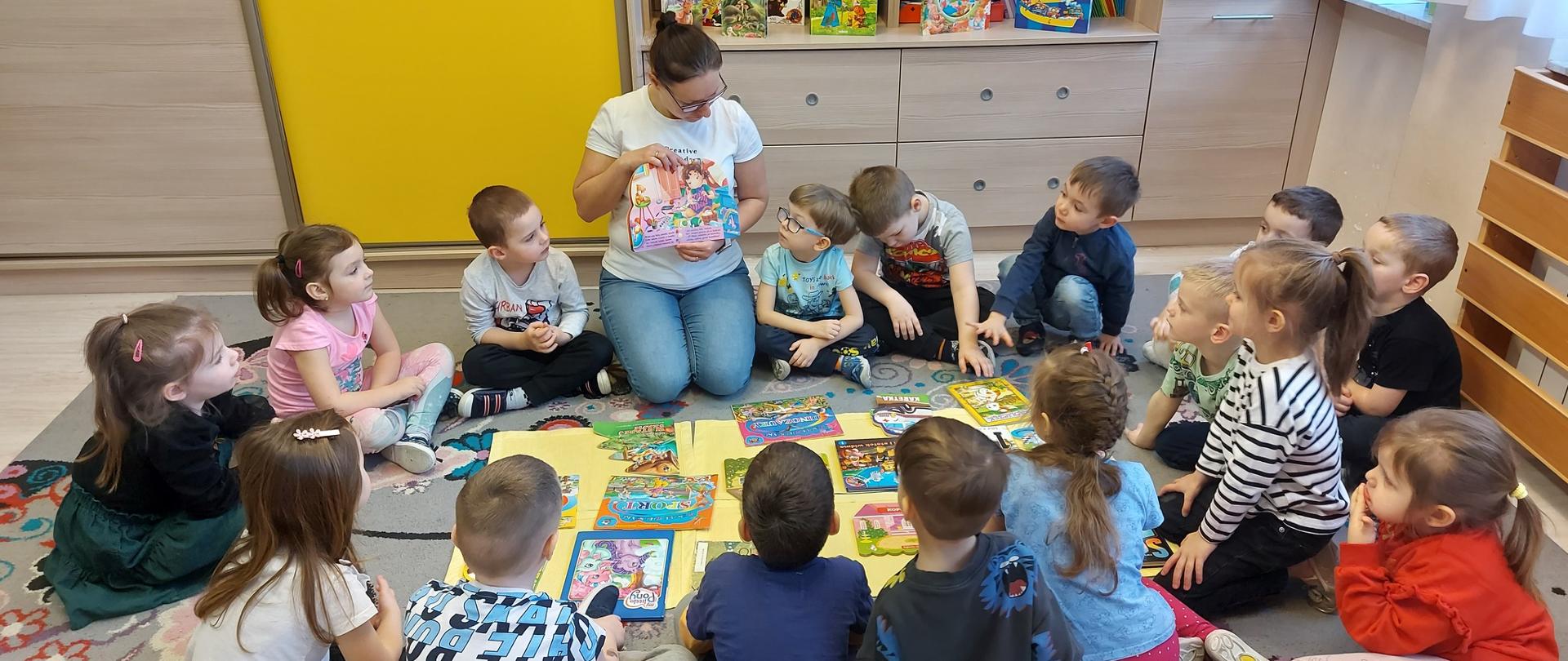 dzieci z nauczycielem siedzą w kręgu. Nauczyciel prezentuje dzieciom książkę 