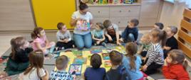 dzieci z nauczycielem siedzą w kręgu. Nauczyciel prezentuje dzieciom książkę 