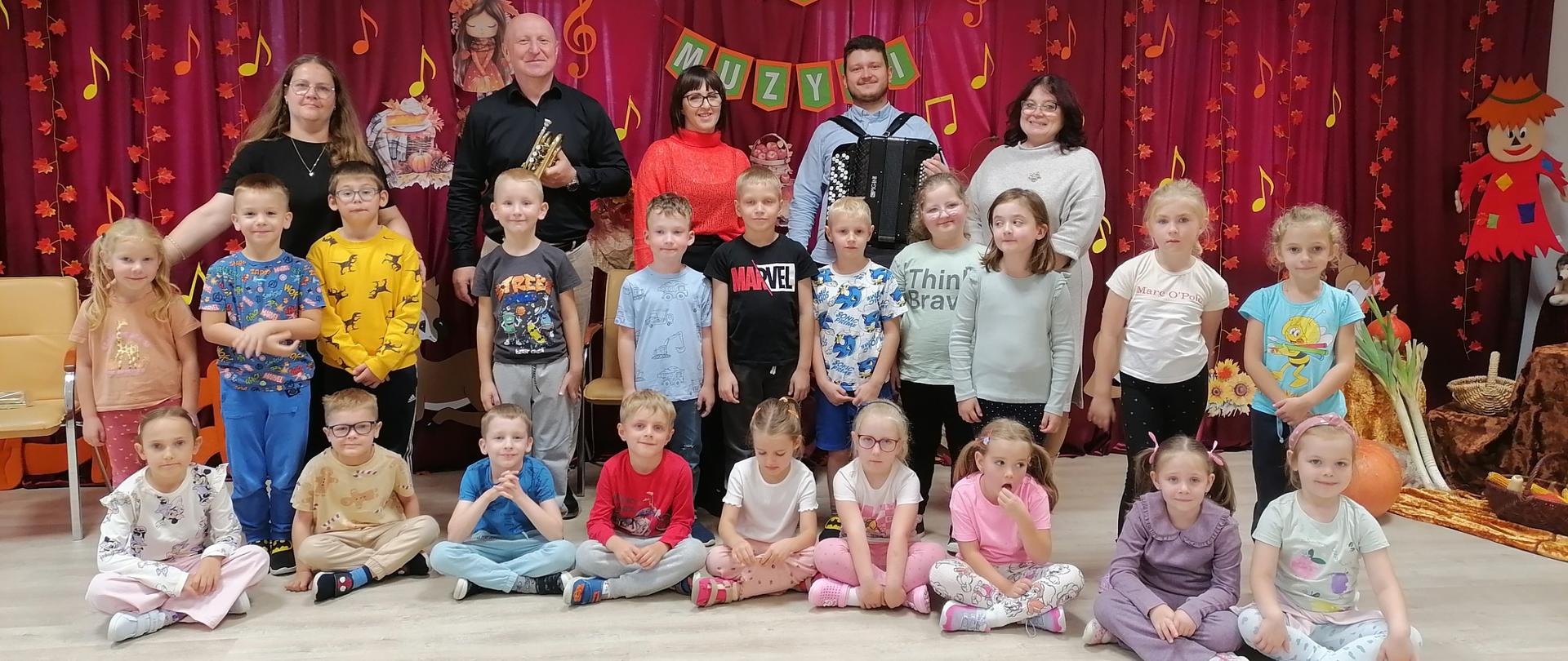 Grupa dzieci i 5 dorosłych na tle napisu Dzień Muzyki 