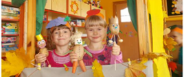 Dwie dziewczynki pozują przy scenie z kukiełkami z warzyw
