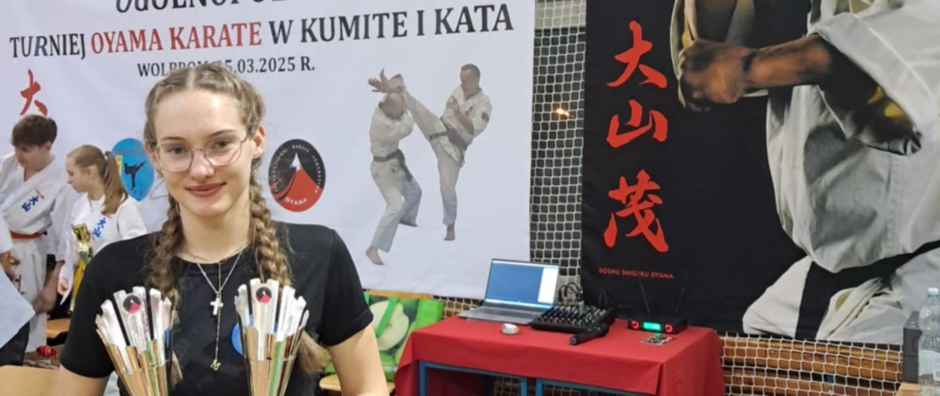 Dziewczyna trzyma dwa puchary w tle zawodnicy karate na plakatach