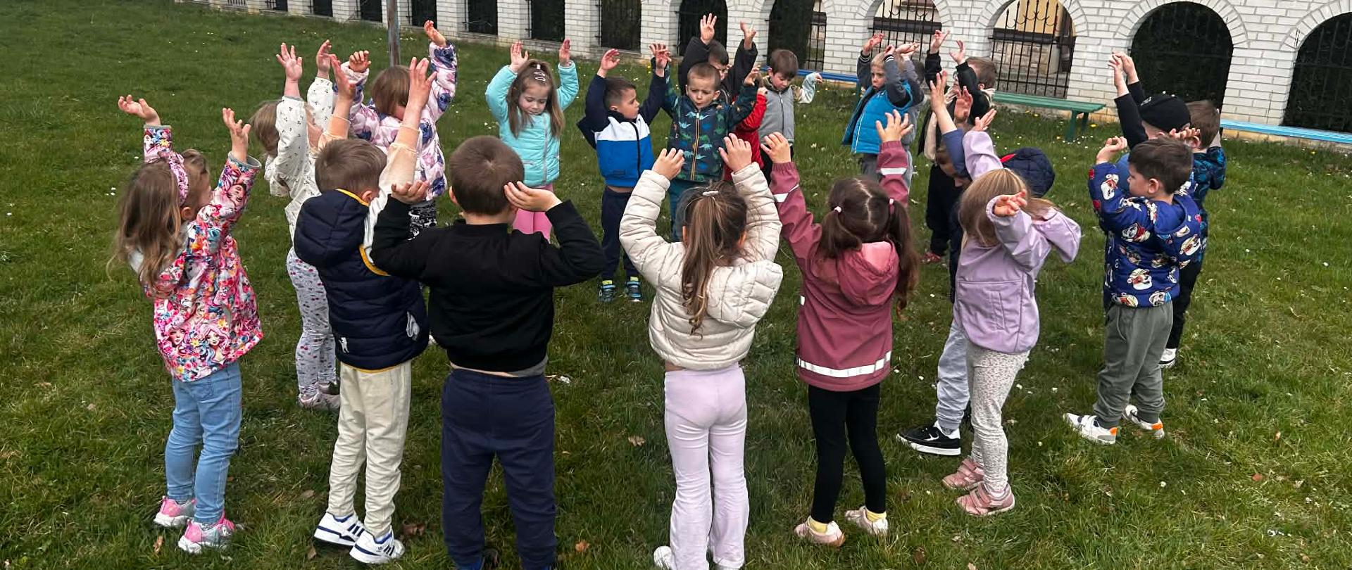 Grupa dzieci wykonuje ćwiczenia gimnastyczne na świeżym powietrzu