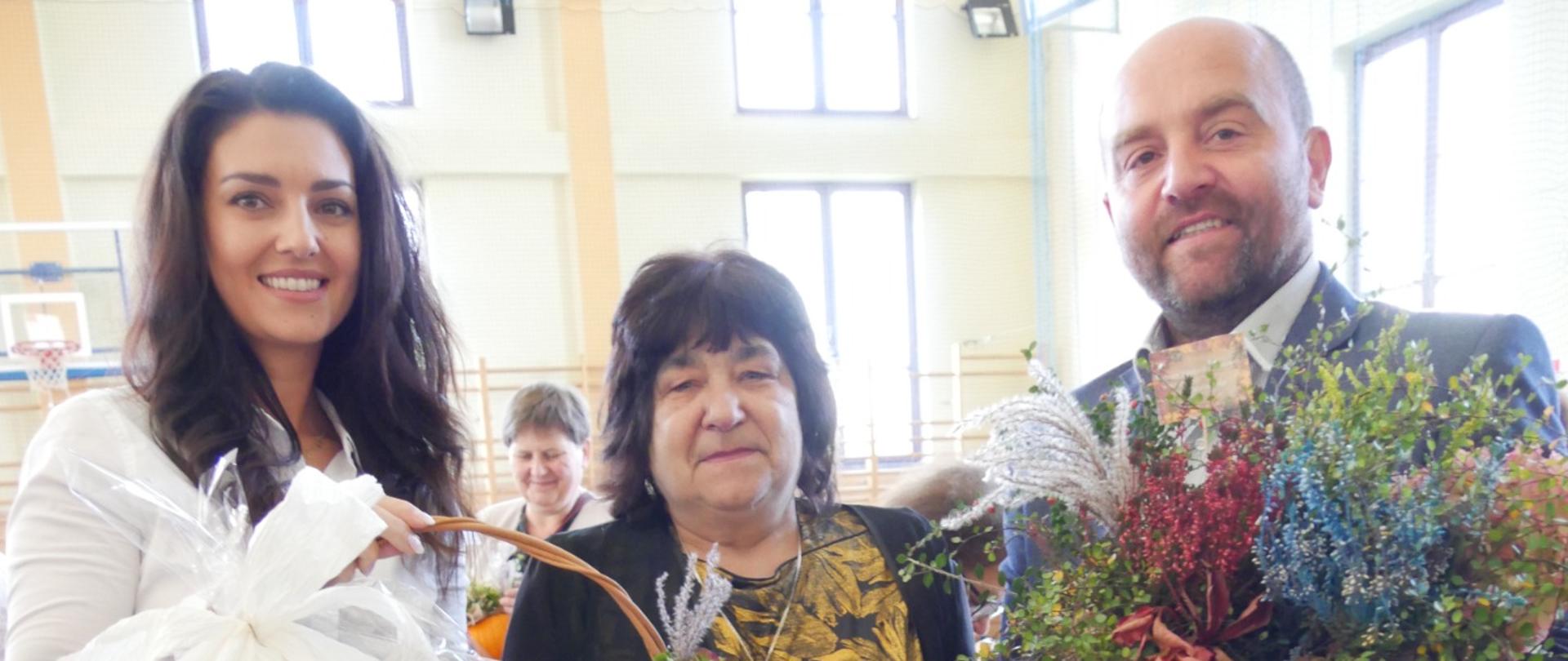 Przedstawiciele Rady Rodziców z koszem kwiatów żegnają nauczyciela odchodzącego na emeryturę.