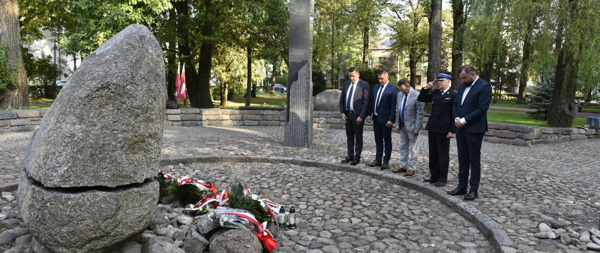 Reprezentanci Powiatu Sokołowskiego stoją przed pomnikiem z pochylonymi głowami po złożeniu kwiatów.