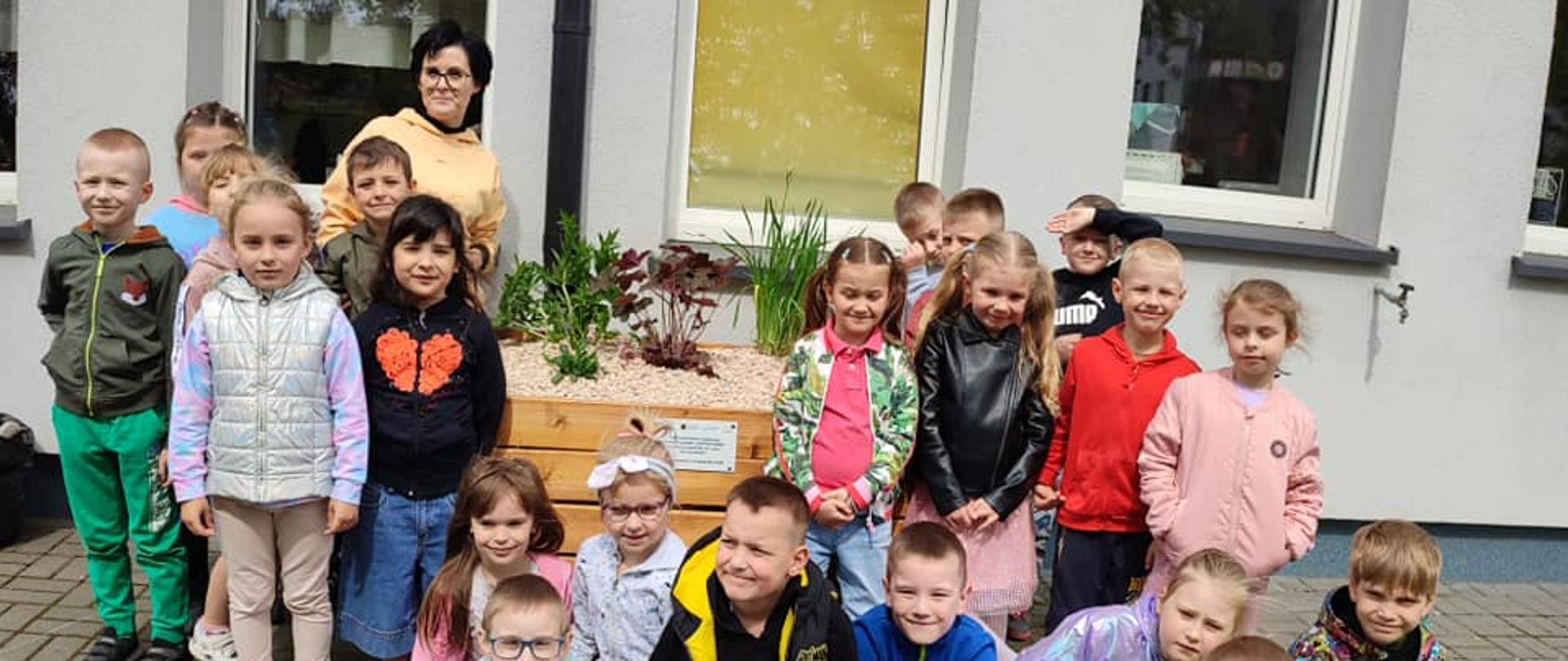 1 dorosły i dzieci przy donicy z roślinami