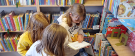 Zdjęcie przedstawia dzieci przeglądające książki w bibliotece, widoczne jest też logo DKK i Instytutu Książki
