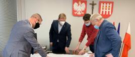 na obrazku w budynku Urzędu Gmina Rutkiod lewej strony stoją: Wicestarosta Zambrowski, Wójt Gminy Rutki, pracownik wydziału IR oraz Naczelnik Wydziału IR w tle widać na ścianie godło, krzyż oraz logo gminy