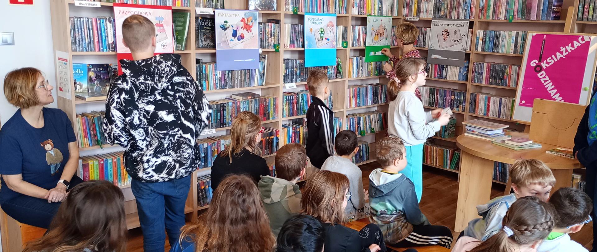 Zdjęcie przedstawia dzieci bawiące się w dopasowywanie obrazków do gatunków literackich.