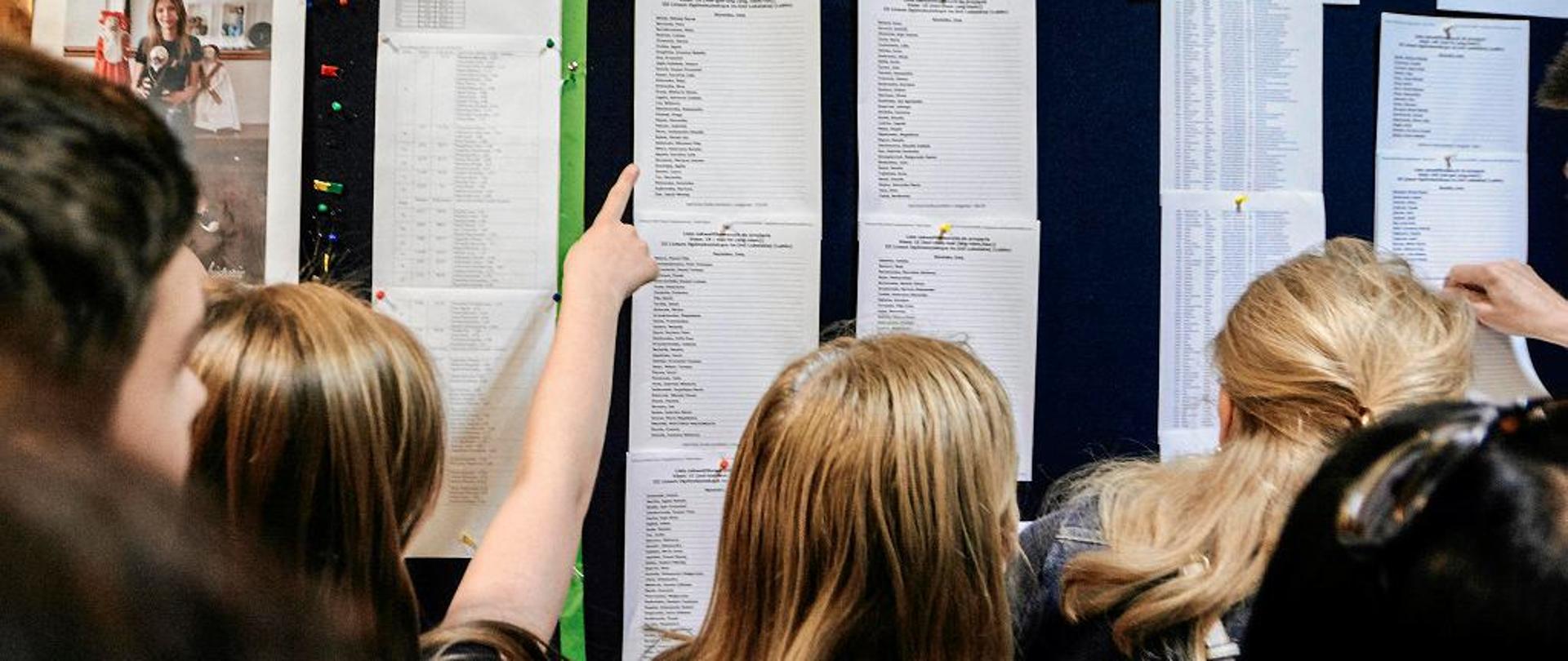 uczniowie sprawdzają listy uczniów przyjętych do szkoły, znajdującą się na tablicy ogłoszeń