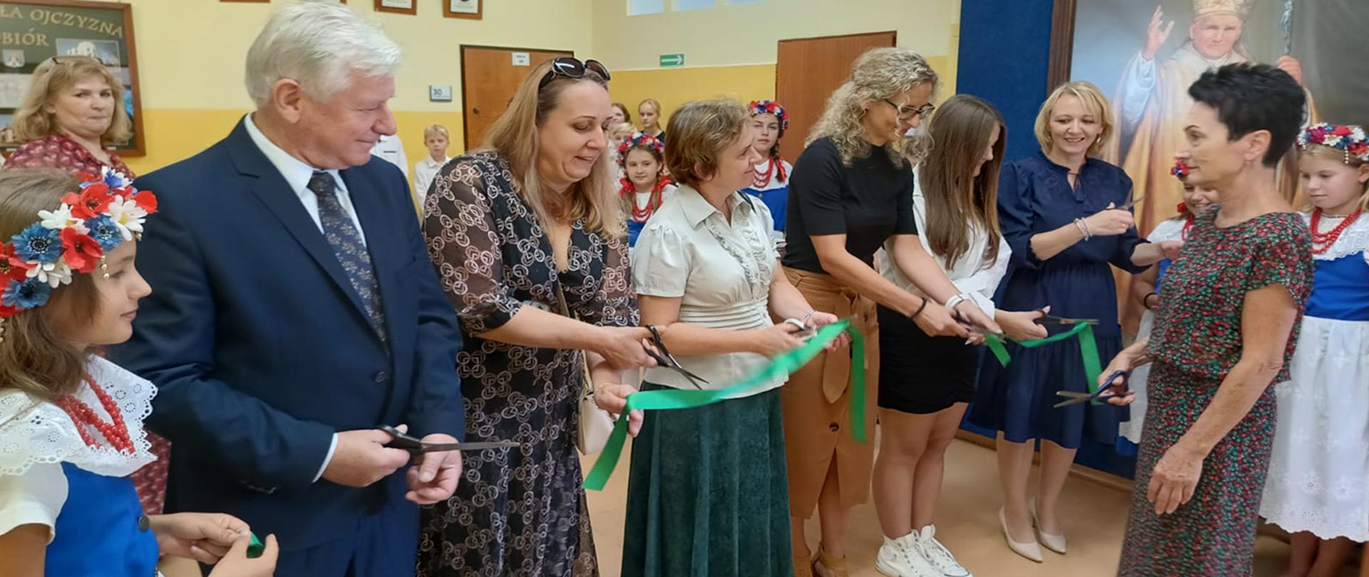 Uczniowie, pracownicy szkoły, pracownicy urzędu gminy, oraz członkowie rady rodziców przecinający zieloną wstęgę.