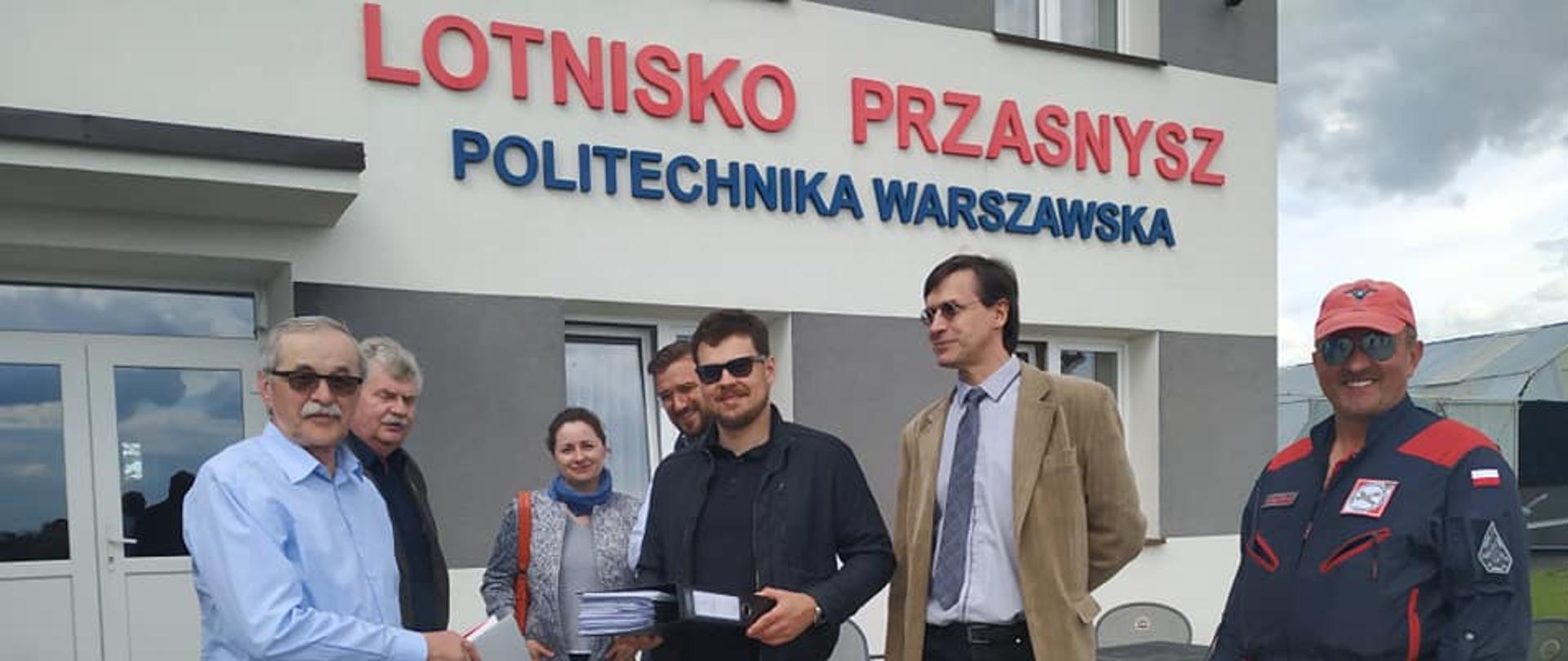 Zdjęcie przedstawia przedstawicieli Lotniska w Sierakowie pod Przasnyszem i Politechniki Warszawskiej wymieniających dokumenty po podpisaniu umowy na budowę laboratorium.