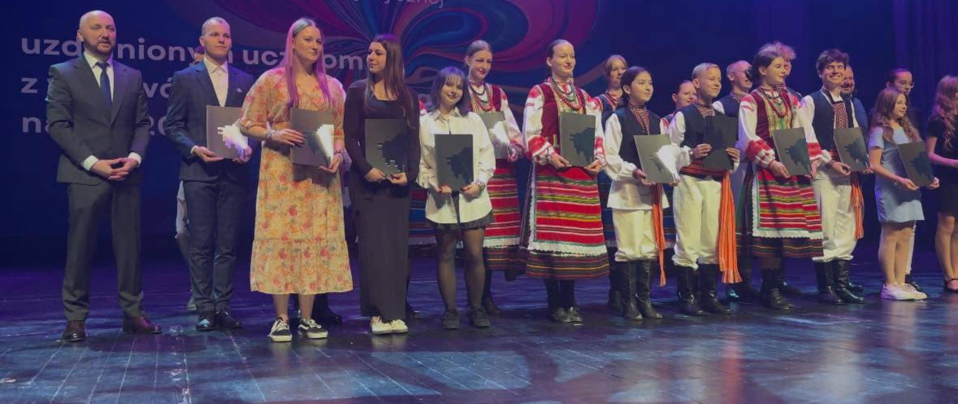 Nagrodzeni uczniowie na scenie pozują do zdjęcia z Marszałkiem Województwa Podlaskiego