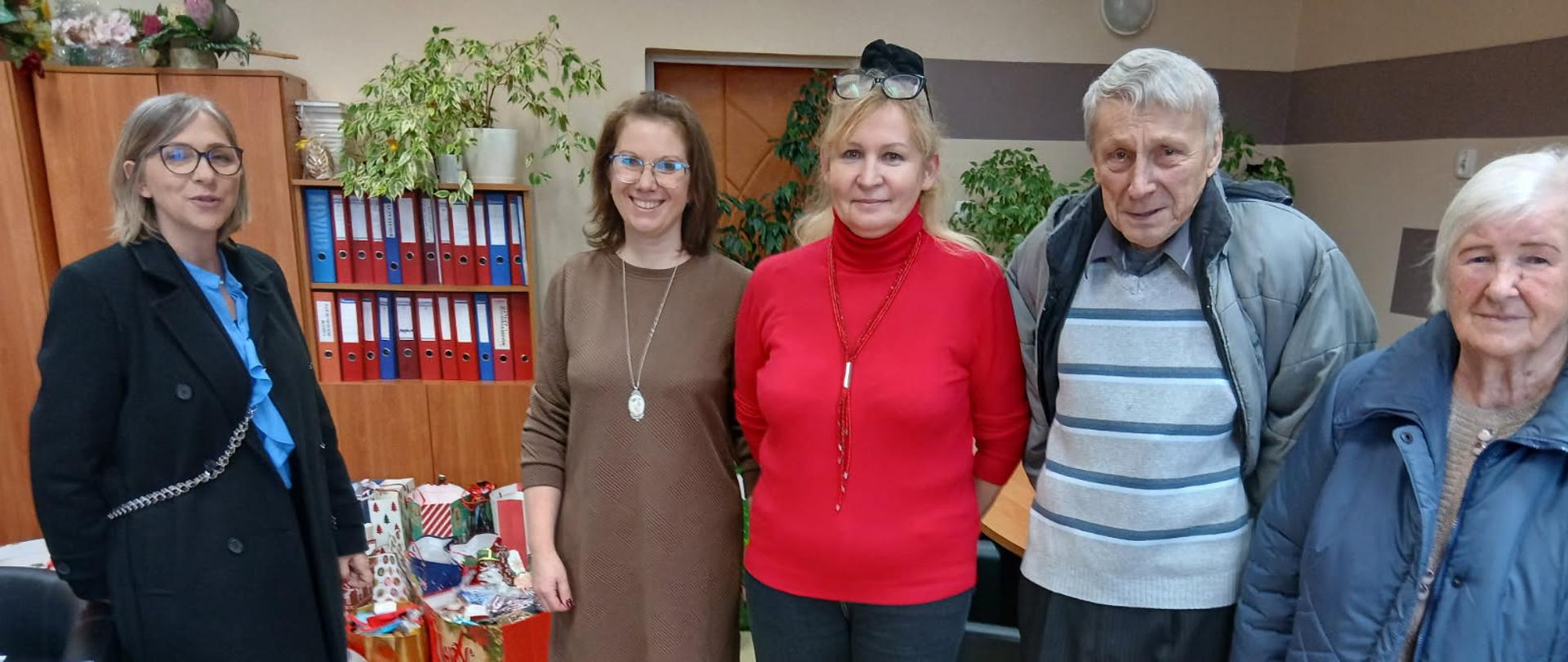 4 kobiety i 1 mężczyzna stoją. Za nimi stoją torby prezentowe