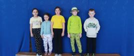 Trzy dziewczynki i dwóch chłopców ubrani w zielone albo żółte koszulki stoją na tle granatowej kotary