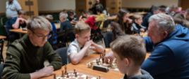 Uczestnicy podczas turnieju - siedzą przy stołach rozgrywają partię szachów