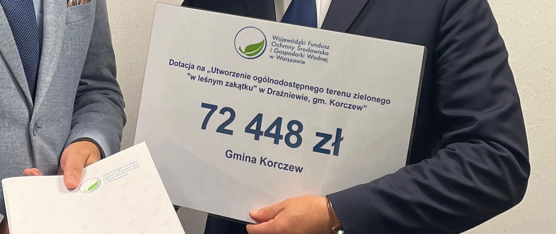 dwóch mężczyzn w garniturach. Jeden trzyma czek z przyznaną kwotą dofinansowania 72 448 zł. 