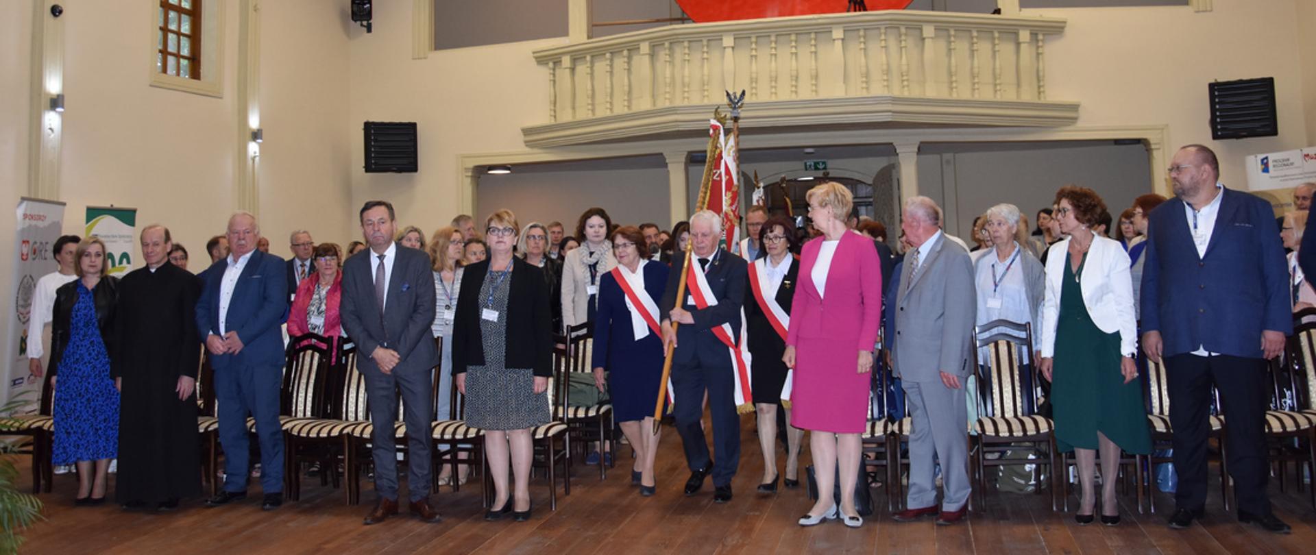 Moment wprowadzenia pocztów sztandarowych, które przechodzą na miejsce spotkania pomiędzy zgromadzonymi w Regionalnym Centrum Kultury w Rozbitym Kamieniu uczestnikami.