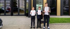 3 uczniów stoi przed budynkiem Akademii Nauk Stosowanych w Nowym Sączu, w której odbywa się rozdanie nagród