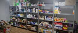 Pomoc humanitarna zorganizowana przez Powiat Przasnyski dla obywateli Ukrainy. Na zdjęciu magazyn z półkami wypełnionymi artykułami spożywczymi i chemii gospodarczej. Na podłodze po lewej stronie zapakowane torby i kartony gotowe do przekazania potrzebującym. 