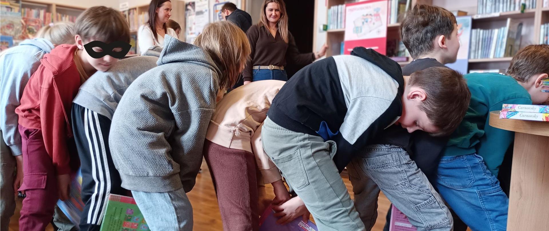 Na zdjęciu widać dzieci ustawione w wężyk i podające sobie książki jedno do drugiego dołem.
