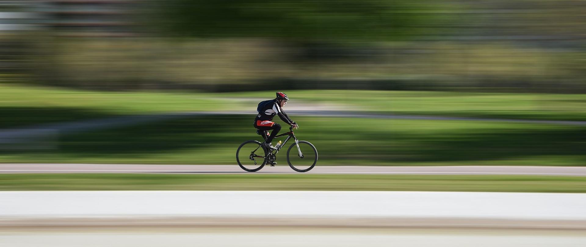Zdjęcie przedstawia jedną osobę jadącą na rowerze na zewnątrz