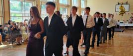 Absolwenci tańczą w parach poloneza na sali gimnastycznej
