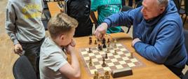 Uczestnicy podczas turnieju - siedzą przy stołach rozgrywają partię szachów