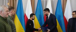 Zdjęcie przedstawia dwie osoby stojące wewnątrz budynku i podające sobie ręce
