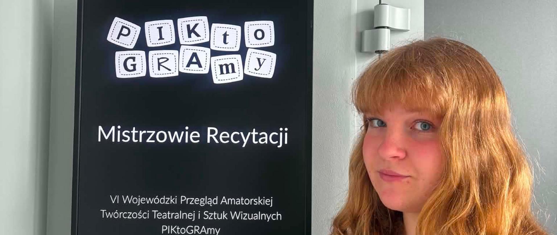 Na zdjęciu znajduje się uczennica biorąca w konkursie PIKTOGRAMY- Sara Korenkiewicz. Obok niej znajduje się tabliczka na której widnieje napis: Mistrzowie Recytacji. VI Wojewódzki Przegląd Amatorskiej Twórczości Teatralnej i Sztuki Wizualnej „PIKtoGRAmy”.