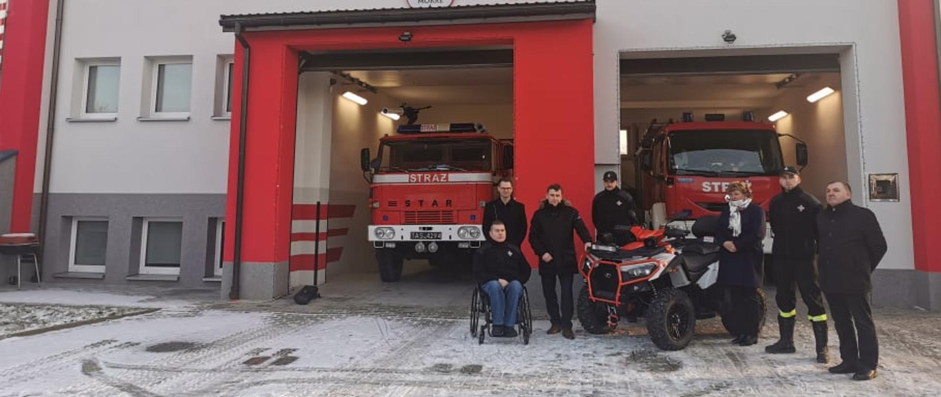 Od lewej Prezes OSP Jadowniki Maciej Mądrzyk, Wójt Gminy Tomasz Banek, Wiceprzewodniczący Sejmiku Województwa Małopolskiego Wojciech Skruch, strażak OSP Jadowniki Mokre, sołtys wsi Jadowniki Mokre Urszula Kogut, strażak OSP Jadowniki Mokre, Przewodniczący Rady Gminy Piotr Moskal.W tle budynek OSP Jadowniki Mokre.