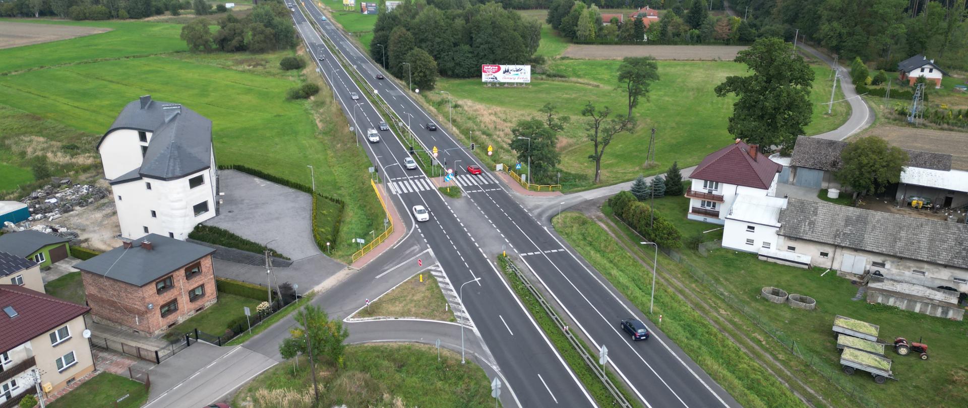 Skrzyżowanie drogi dwupasmowej z jednopasmową wokół domki jednorodzinne łąki i lasy