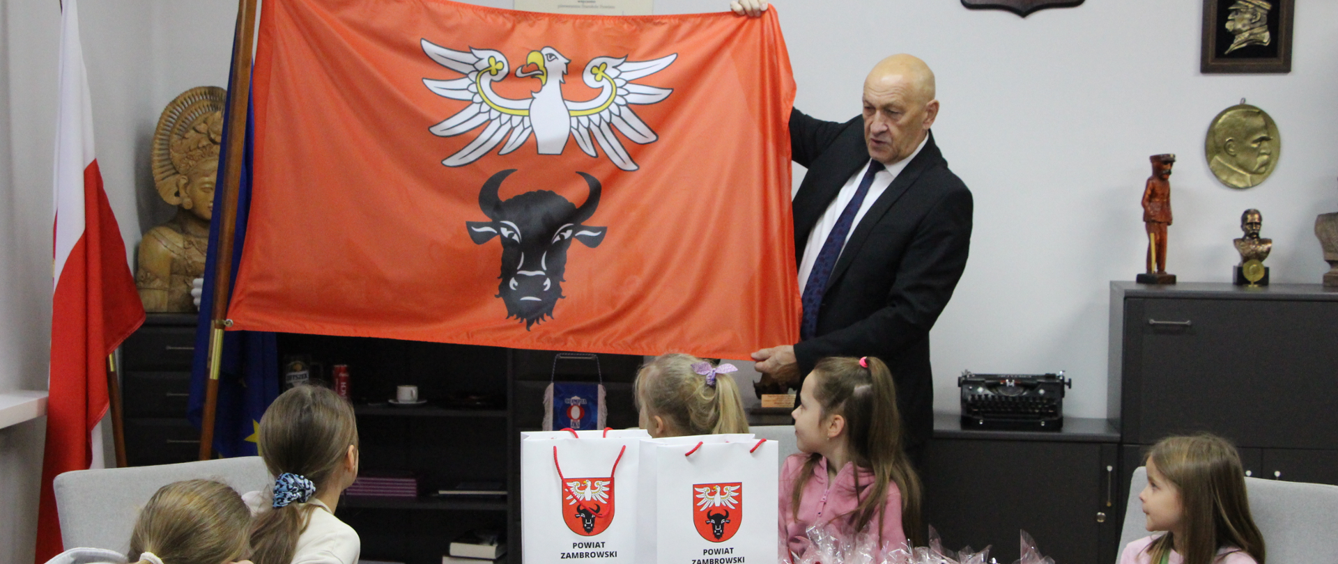 Starosta Zambrowski pokazuje dzieciom flagę powiatu zambrowskiego