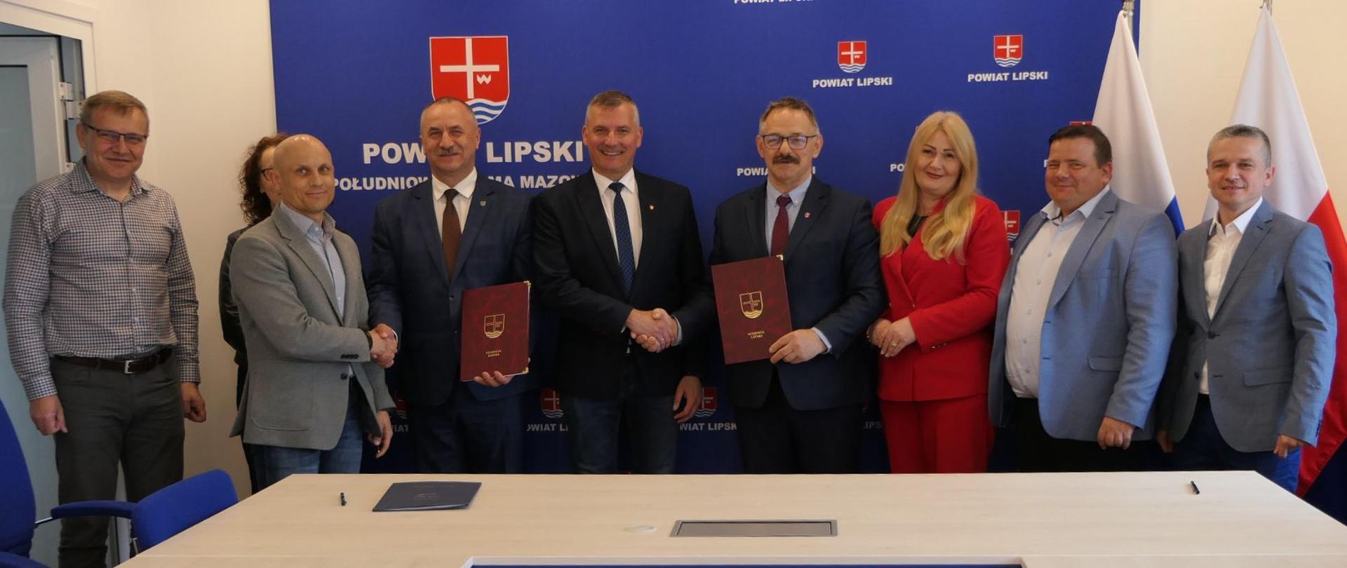 Uczestnicy wydarzenia. W tle granatowa ścianka z herbem Powiatu Lipskiego.
