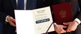ręce trzymające otwartą teczkę z informacją o źródle i kwocie dofinansowania.