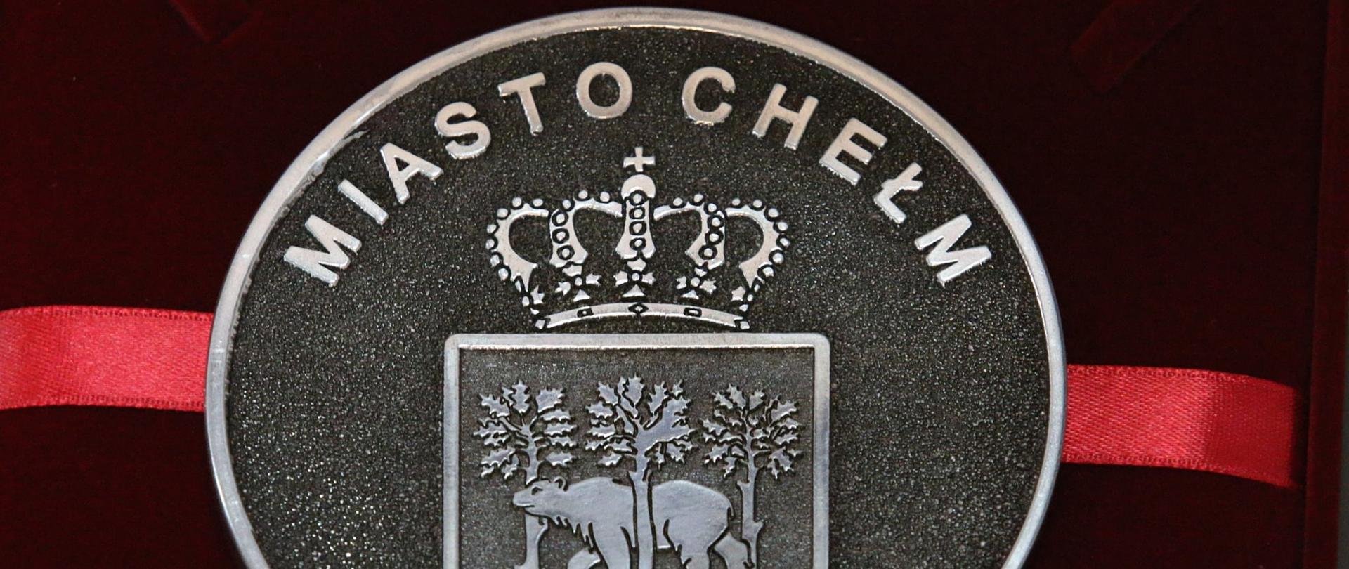 Tłoczony ze stali medal dla Chełmianina Roku. Widać na nim herb miasta (niedźwiedź pomiędzy trzema dębami), a nad herbem napis "Miasto Chełm".