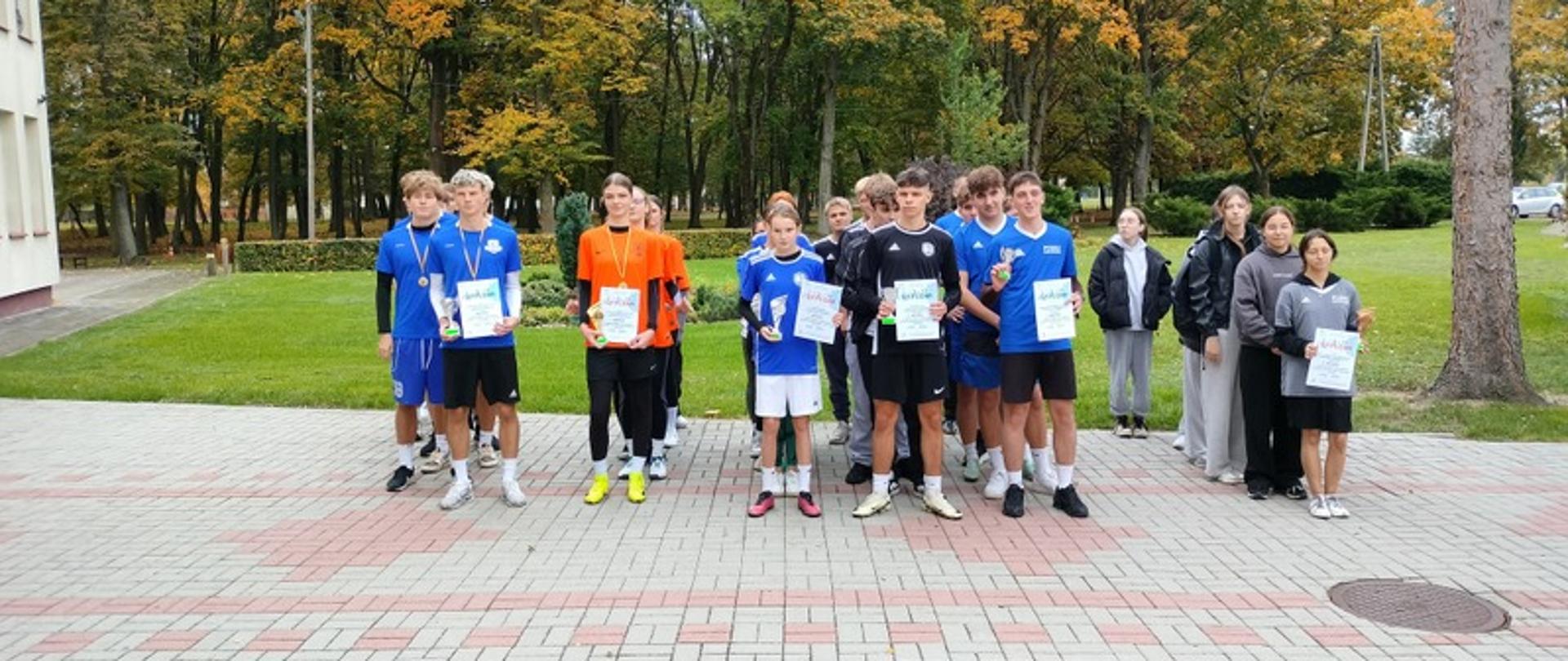 Grupowe zdjęcie uczestników Powiatowej Licealiady w Jesiennych Sztafetowych Biegach Przełajowych po wręczeniu pucharów, medali i dyplomów
