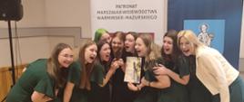 Dziewczyny w zielonych sukienkach preznetują nagrody i dyplomy